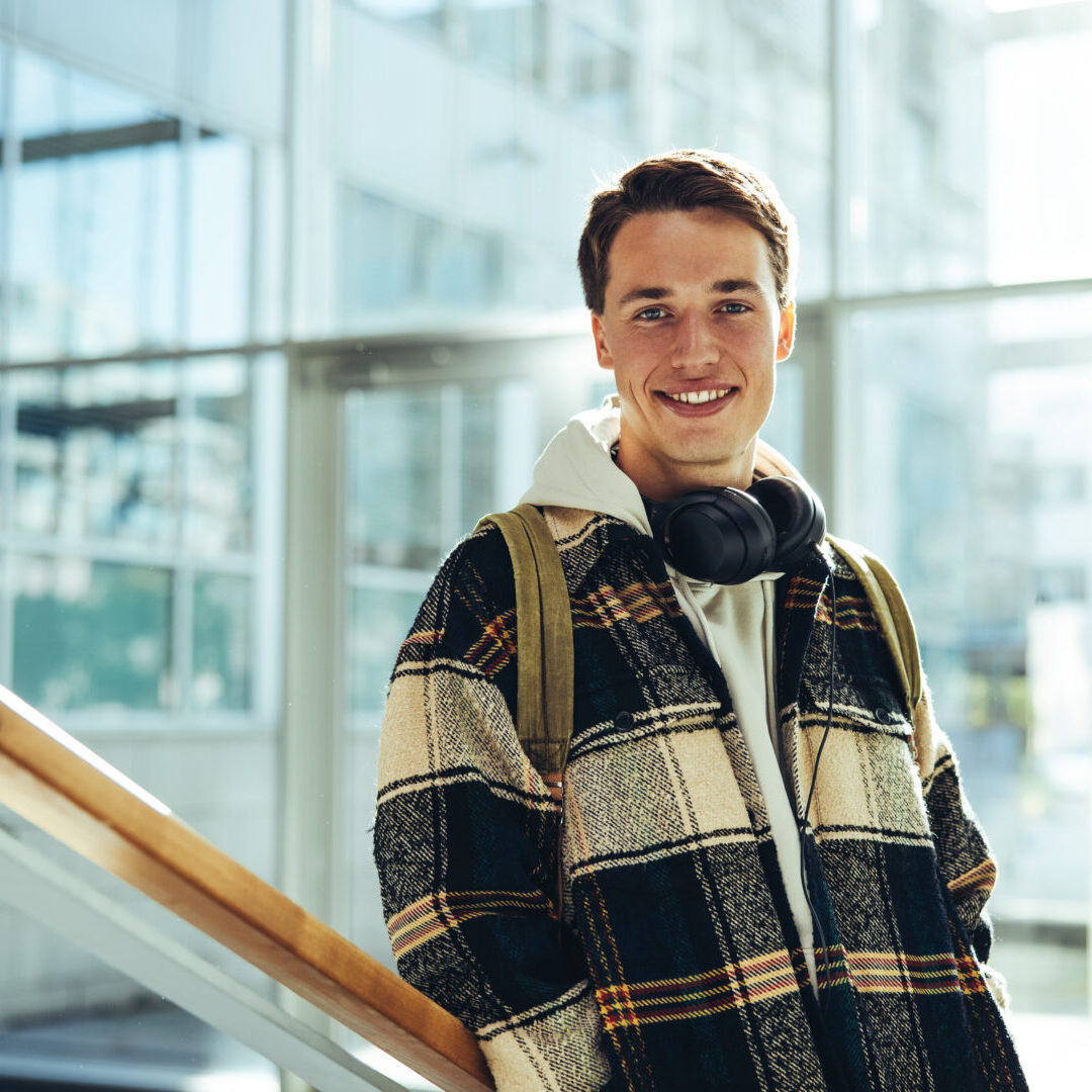 Student at college stairs smiling. Young man smiling at camera while leaning at stairs railing in university.